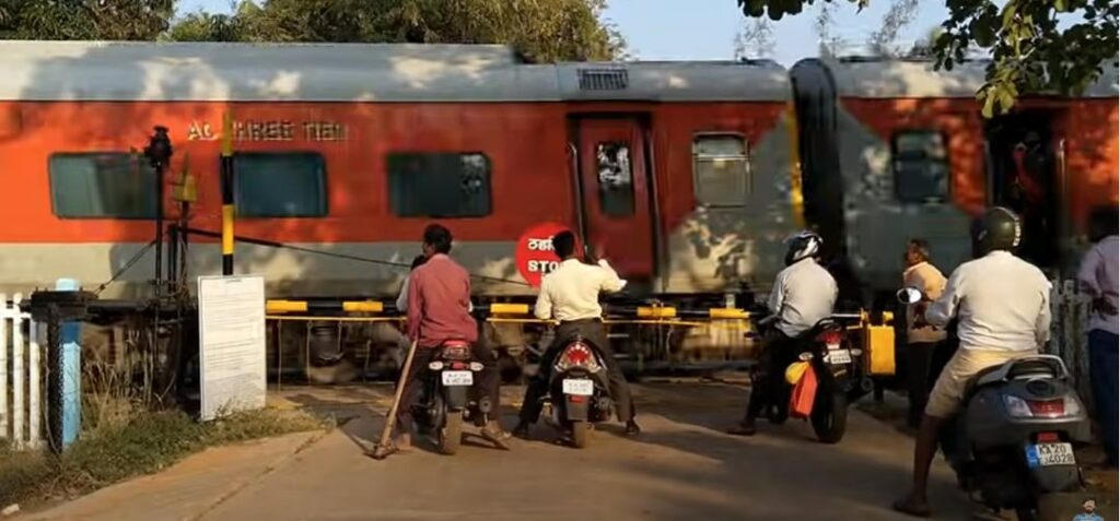 Motorcyclists waiting at the Wardha–Sevagram railway level crossing as an Indian Railways AC Three Tier train passes. The crossing that stood between home and the 8 am class at MGIMS.