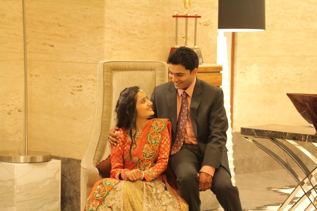 Amrita and Sahaj sitting together; Amrita is wearing a vibrant orange and gold lehenga while Sahaj is in a charcoal grey suit.