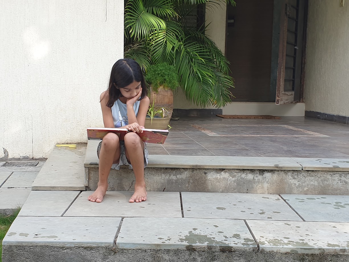 Diti, age thirteen, reading a book on the porch steps, June 2021
