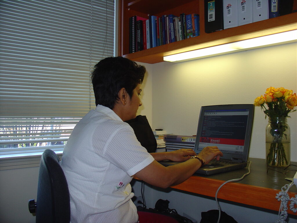 Bhavana Kalantri at the study desk in Dr. S.P. Kalantri's studio apartment at 2100 Channing Way, Manville, Berkeley, California, December 2004. Public health textbooks visible on the shelf above. Bhavana visited for three weeks during the Christmas vacation while Dr. Kalantri was completing his MPH at UC Berkeley.
