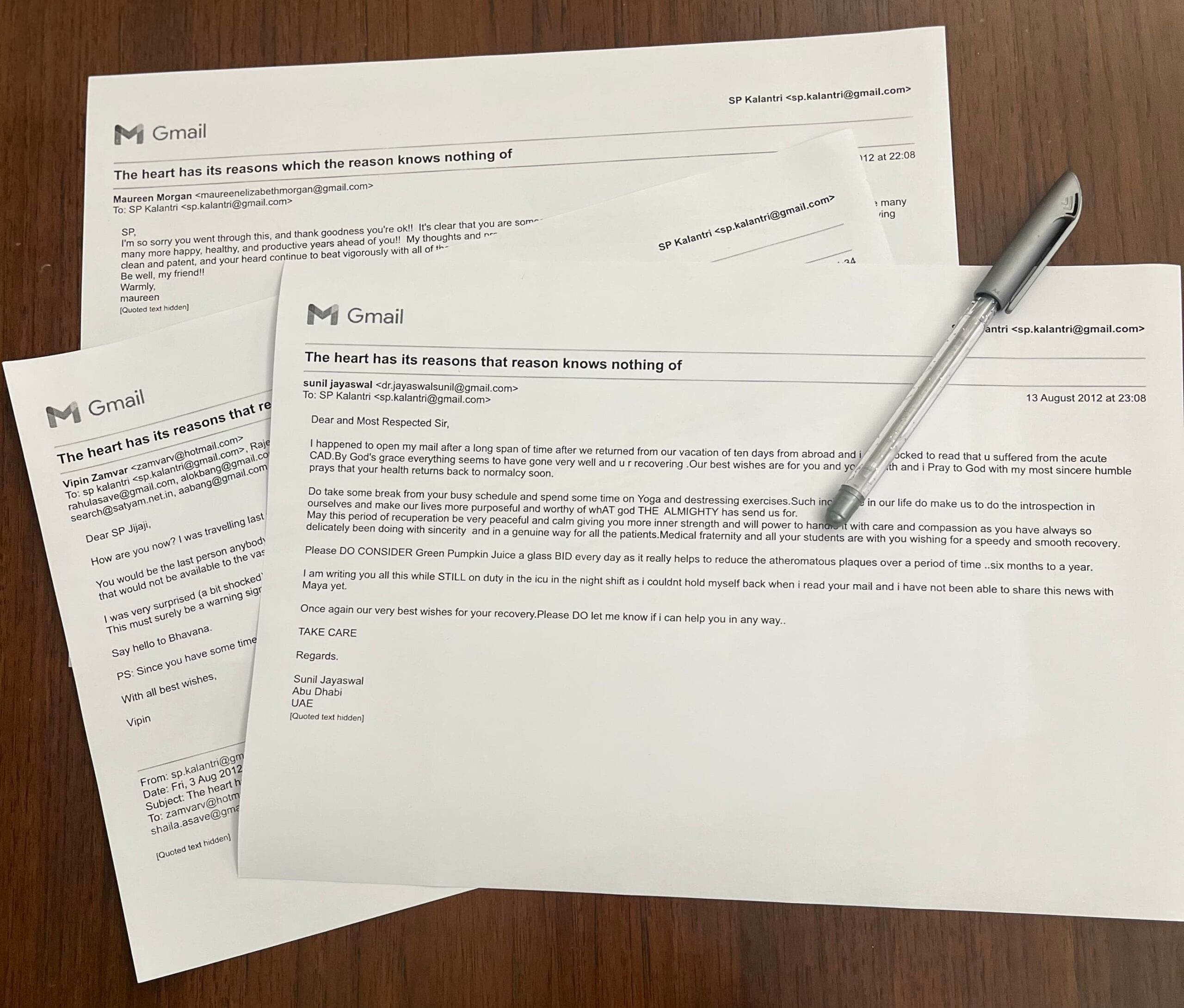Three printed Gmail letters received by Dr. S.P. Kalantri from former students and colleagues after his first heart attack in July 2012, lying overlapping on a wooden surface with a pen resting across them.