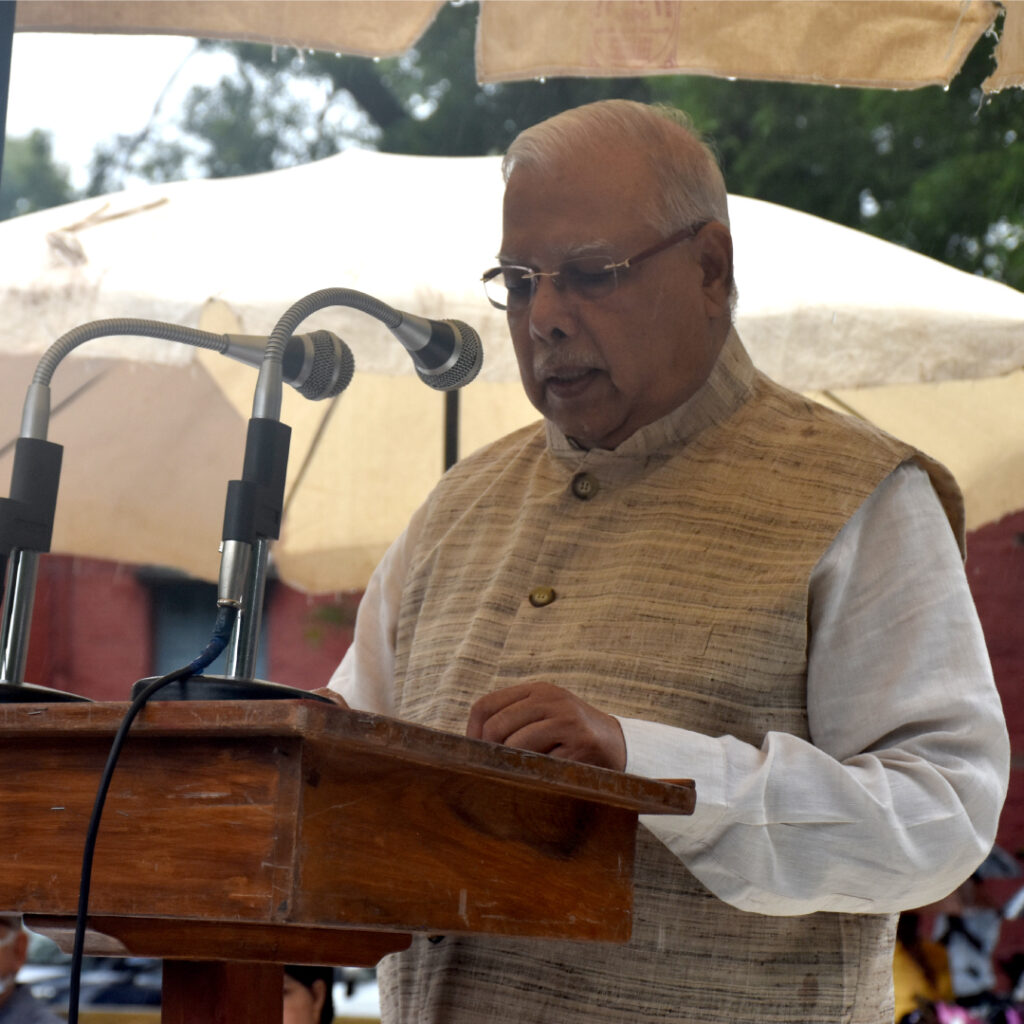 Mr. PL Tapdiya, President of Kasturba Health Society, delivering a speech at a wooden podium.