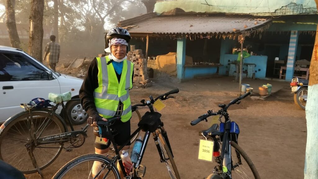 SP Kalantri at the midpoint of the 300km Nagpur to Deori brevet, late afternoon, after eleven hours of non-stop cycling, 2017. High-visibility vest, helmet, face covering, rider number tags on bicycle.